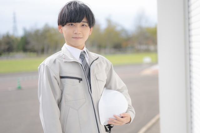 ヘルメットを手に持つ作業服を着た男性の写真