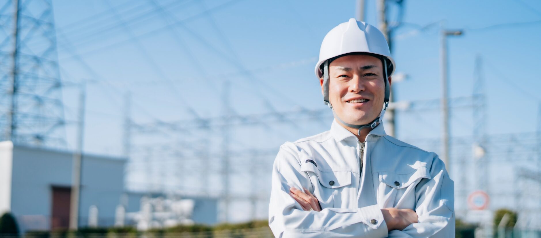 鉄塔や高架線を背景にこちらを見てほほ笑む作業員の写真